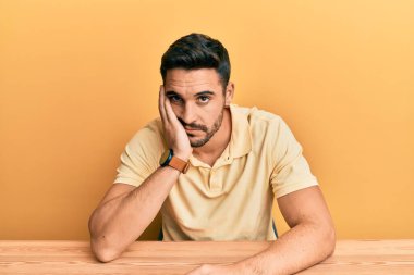 Gündelik kıyafetler giyen genç İspanyol adam masaya oturmuş kollarını kavuşturup depresyondan sıkılmış ve yorgun göründüğünü düşünüyor.. 