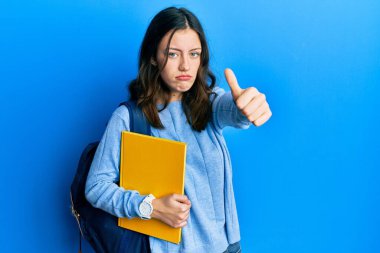 Sırt çantası takan esmer, genç bir kız öğrenci. Depresyona girmiş, üzgün ve korkmuş bir şekilde el hareketi yapıyor. hüzünlü ifade. 