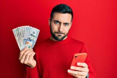 Akıllı telefon kullanan genç bir İspanyol, Amerikan dolarlarını elinde tutuyor şüpheci ve sinirli, sorun yüzünden surat asıyor. negatif kişi. 