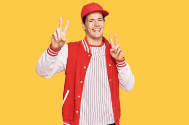 Beyzbol üniforması giyen yakışıklı beyaz adam kameraya bakıp zafer işareti yapıyor. İki numara.. 