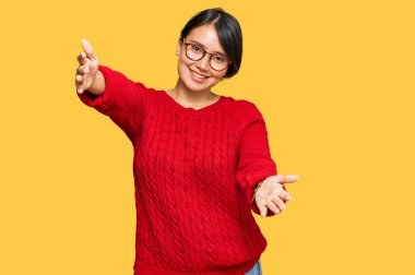 Kısa saçlı, sıradan süveter giyen ve gözlüklü genç, güzel İspanyol kadın kameraya bakıp sarılmak için gülümsüyor. Mutluluğu kucaklayan neşeli bir ifade.. 