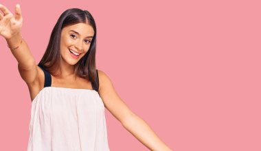 Gündelik giysiler giymiş genç İspanyol kadın kameraya bakıp sarılmak için kollarını açmış gülümsüyor. Mutluluğu kucaklayan neşeli bir ifade.. 