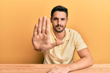 Gündelik giysiler giymiş genç İspanyol bir adam masada oturuyor ve avuç içiyle şarkı söylemeyi kesiyor. Yüzünde olumsuz ve ciddi bir jest olan uyarı ifadesi. 