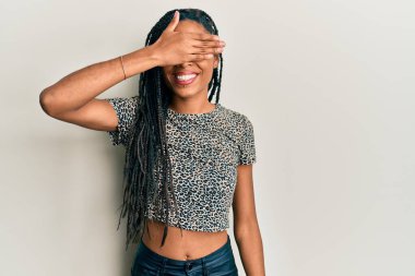 Afro-Amerikalı kadın, günlük kıyafetler giyip, gülümsüyor ve elleri yüzlerinde, şaşırtmak için gözlerini kapatıyor. kör kavram. 