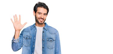 Gündelik kıyafetler giyen genç İspanyol adam beş numarayı gösterip işaret ederken kendinden emin ve mutlu bir şekilde gülümsüyor.. 