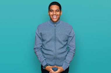 Genç, yakışıklı, sıradan bir kazak giyen ve kameraya seksi bir ifadeyle, neşeli ve mutlu bir yüzle bakan İspanyol bir adam.. 