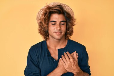 Yaz şapkası takan, elleri göğsünde, gözleri kapalı gülümseyen ve yüzünde minnet ifadesi olan genç bir İspanyol. sağlık kavramı. 