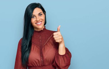 Gündelik giysiler giymiş, mutlu ve pozitif gülümseyen genç beyaz bir kadın. Başparmağıyla mükemmel ve onay işareti yapıyor. 