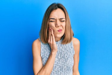 Kafkasyalı genç sarışın kadın diş ağrısı ya da diş hastalığından dolayı gündelik tişört giyip ağızlarına acı dolu bir ifadeyle dokunuyor. dişçi 