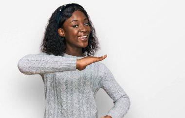 Beautiful african young woman wearing casual winter sweater gesturing with hands showing big and large size sign, measure symbol. smiling looking at the camera. measuring concept. 