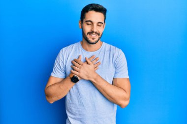 Gündelik kıyafetler giyen genç İspanyol adam elleri göğsünde gülümsüyor, gözleri kapalı ve yüzünde minnet ifadesi var. sağlık kavramı. 