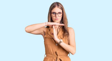 Genç, güzel, sarışın, gündelik kıyafetler ve gözlük takan, el kol hareketi yapan, hayal kırıklığına uğramış ve ciddi yüzlü bir kadın. 