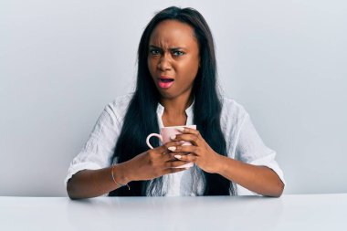 Genç Afrikalı bir kadın şok olmuş suratıyla kahve içiyor. Şüpheci ve alaycı görünüyor. 