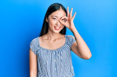 Genç Çinli kadın, sıradan çizgili tişört giyiyor. El hareketleriyle gülümsüyor. Gözleri, mutlu yüzüyle parmaklarının arasından bakıyor.. 