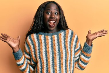 Yün kazak giyen Afrikalı genç bir kadın zaferi mutlu bir gülümsemeyle ve kazanan ifadeyle kutluyor. 