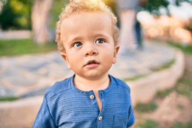 Sevimli ve mutlu küçük çocuk güneşli bir günde parkta eğleniyor. Güzel sarı saçlı erkek çocuk dışarıda oynuyor.