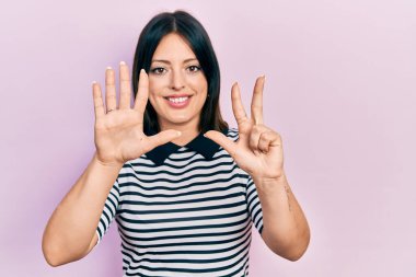 Genç İspanyol kadın gündelik kıyafetler giyer ve sekiz numaralı parmaklarıyla gülümseyerek mutlu ve kendinden emin bir şekilde işaret eder.. 