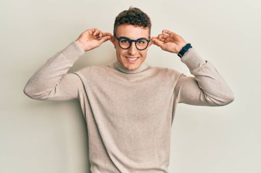 Balıkçı yaka kazak giyen İspanyol genç adam gülümsüyor kulakları parmaklarıyla çekiyor, komik bir jest. deneme sorunu 