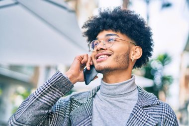 Genç Afrikalı Amerikalı iş adamı gülümsüyor. Şehirdeki akıllı telefondan mutlu bir şekilde konuşuyor..
