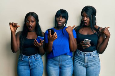 Üç Afro-Amerikalı arkadaş akıllı telefon kullanıyor. Elle işaret ederek şaşırdılar. Ağzını açıp hayrete düştüler.. 