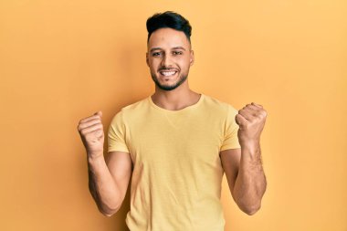 Genç Arap adam gündelik giysiler giyiyor. Çok mutlu ve heyecanlı. Kazanan jest yapıyor, kolları havada, gülümsüyor ve başarı için bağırıyor. kutlama konsepti. 