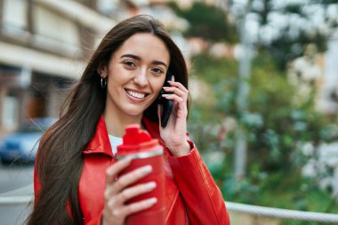 Genç İspanyol kadın akıllı telefondan konuşuyor ve şehirde kahve içiyor..