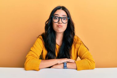 Güzel, esmer, gözlüklü, sıradan elbiseli bir kadın masada oturmuş komik suratıyla yanaklarını şişiriyor. Havayla şişmiş ağız, çılgın bir ifade.. 