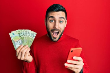 Genç İspanyol adam akıllı telefon kullanıyor Şili pezosu tutuyor çılgınlığı kutluyor ve şaşırıyor gözleri açık heyecanla bağırıyor. 