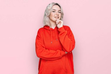 Sıradan kıyafetler giyen genç sarışın kız kameraya özgüvenli bakıyor kollarını kavuşturup gülümseyerek ve çenesini kaldırarak. Olumlu düşünmek. 