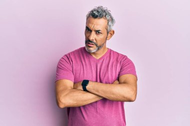 Orta yaşlı, gri saçlı, sıradan kıyafetler giyen şüpheci ve gergin, yüzünde çapraz kollu tasvip etmeyen bir ifade. negatif kişi. 