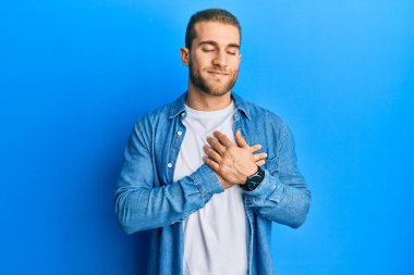 Sıradan kıyafetler giyen, göğsünde elleri, yüzünde minnet dolu bir jestle gülümseyen genç beyaz bir adam. sağlık kavramı. 