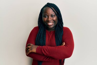 Saçları örgülü, mutlu yüzlü, kolları çaprazlanmış, kameraya bakan genç siyahi bir kadın. pozitif kişi. 