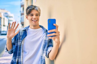 Genç İspanyol gülümseyen adam şehirde akıllı telefon kullanarak video araması yapıyor..