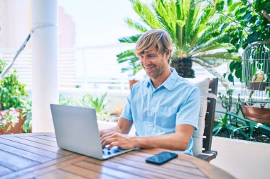 Evde bilgisayar laptopu kullanan orta yaşlı yakışıklı bir adam.