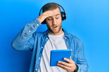 Kulaklık takan genç, beyaz bir adam. Stresli ve hayal kırıklığına uğramış, şaşırmış ve sinirli bir yüzü var. 