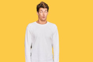 Beyaz bir süveter giyen yakışıklı beyaz bir adam dudaklarıyla balık suratı yapıyor, çılgınca ve komik bir jest. Komik ifade. 