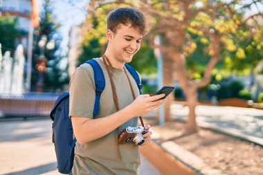 Kafkasyalı genç turist şehirde klasik akıllı telefon kullanarak mutlu bir şekilde gülümsüyor..