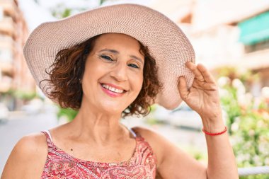 Tatilde olan orta yaşlı bir kadın yaz stili giyinmiş şehrin caddesinde yürüyor..