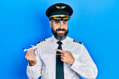 Pilot üniforması giyen genç İspanyol adam uçak oyuncağı tutuyor. Gülümsüyor, mutlu bir şekilde eli ve parmağı işaret ediyor. 