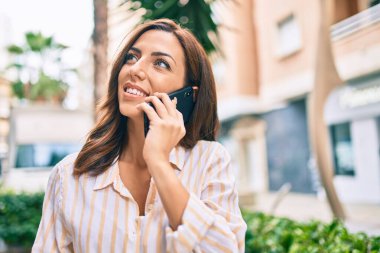 Genç İspanyol kadın gülümsüyor. Şehirdeki akıllı telefondan konuşuyor..