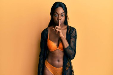Genç Afro-Amerikalı kadın iç çamaşırı giyip dudaklarında parmaklarıyla sessiz olmak istiyor. sessizlik ve gizli konsept. 