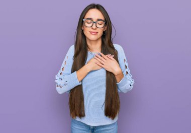 Gündelik kıyafetler ve gözlük takan genç İspanyol kız elleri göğsünde, gözleri kapalı ve yüzünde minnet dolu bir jest ile gülümsüyor. sağlık kavramı. 