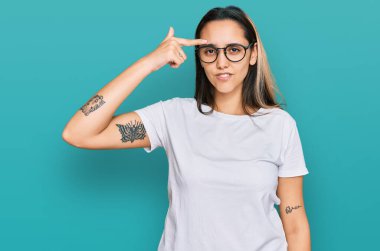 Sıradan beyaz tişört giyen genç İspanyol kadın alnındaki sivilceden mutsuz olduğunu gösteriyor. Siyah noktalı çirkin bir enfeksiyon. sivilce ve deri problemi 