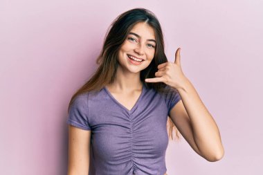 Sıradan kıyafetler giyen, gülümseyen, el ve parmaklarıyla telefon hareketi yapan, telefonda konuşan beyaz bir kadın. iletişim kavramları. 