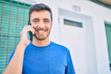 Genç beyaz adam gülümsüyor. Şehirdeki akıllı telefondan konuşuyor..