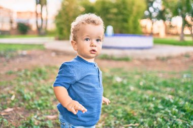 Sevimli ve mutlu küçük çocuk güneşli bir günde parkta eğleniyor. Güzel sarı saçlı erkek çocuk dışarıda oynuyor.