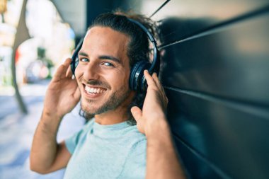 Genç İspanyol gülümseyen adam şehirde kulaklık takarak müzik dinlemekten mutlu oluyor..