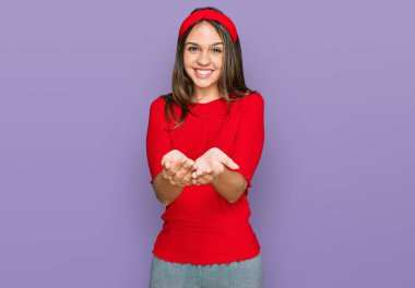 Elleri avuçlarında gülümseyen, sıradan kıyafetler giyen esmer bir kadın el hareketi yapıyor. Bekleme ve koruma 