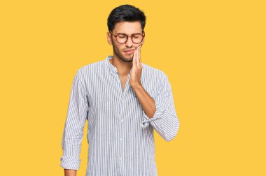 Sıradan kıyafetler giyen ve gözlük takan genç yakışıklı bir adam diş ağrısı ya da diş hastalığından dolayı acı dolu bir ifadeyle ağıza dokunuyor. dişçi 