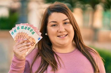 Genç İspanyol artı iri kadın gülümseyerek şehirde 10 avroluk banknotlar tutuyor..